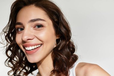 Zarif makyajlı neşeli bir kadın şık bir stüdyo ortamında rahatça poz verir..