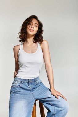 Güzel bir kadın, gri bir arkaplana karşı zahmetsizce makyaj yaparak poz verir, zarafet saçar..