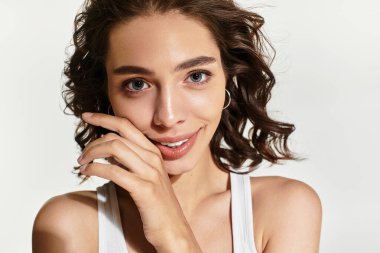 Genç bir kadın stüdyoda poz veriyor, göz kamaştırıcı makyajını ve kıvırcık saçlarını doğal ışıkta gösteriyor..