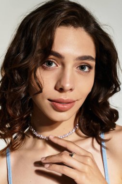 Göz kamaştırıcı makyajlı genç bir kadın gri bir zemine karşı zarifçe poz veriyor..