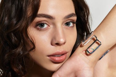 Zarif makyajlı genç bir kadın zarif bir şekilde gri bir arkaplanda poz veriyor, güzelliğini ön plana çıkarıyor..