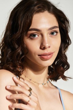 Kusursuz makyajlı genç bir kadın stüdyoda gri bir zemine karşı zarifçe poz veriyor..