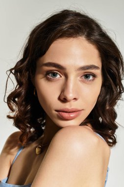 Parlak makyajlı genç bir kadın stüdyo ortamında zarifçe poz veriyor ve güzelliğini ön plana çıkarıyor..