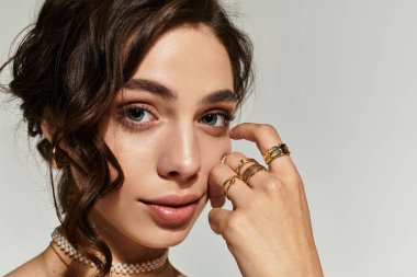 Zarif makyajlı güzel bir genç kadın zarif bir şekilde gri bir arkaplanda poz veriyor..