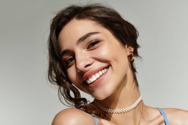 Güzel makyajlı genç bir kadın, parlak gülüşünü stüdyo ortamında sergiliyor..