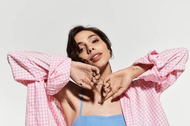 Genç bir kadın, mavi bir yaz elbisesiyle, tarafsız bir arkaplanda zarif bir şekilde poz verir..