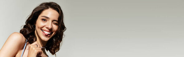 Молодая женщина с потрясающим макияжем радостно позирует в студии на сером фоне, баннер