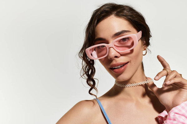 Молодая женщина уверенно позирует в синем летнем платье и стильных солнечных очках в студии.