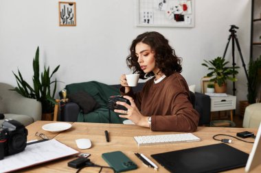 Kıvırcık saçlı serbest yazar, rahatlamış çalışma alanındaki kamera ayarlarını incelerken kahvenin tadını çıkarıyor..