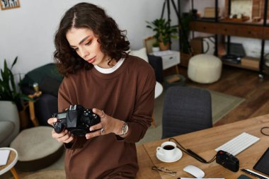 Odaklanmış genç bir kadın şık ofis düzeninde çalışırken kamerasını inceliyor..