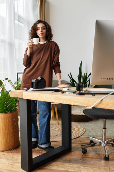 Young woman with curly hair sips coffee at her home office, capturing moments as a photographer.