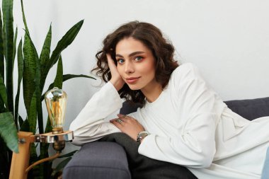 Kıvırcık kahverengi saçlı güzel genç bir kadın modern dairesinde biraz dinleniyor..