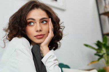 Kıvırcık kahverengi saçlı genç bir kadın şık dairesinde dinleniyor, huzur saçıyor..