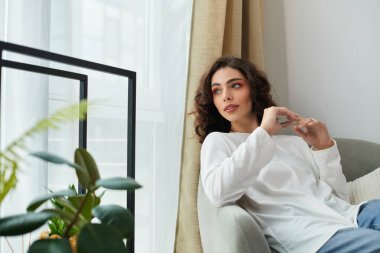 Kıvırcık saçlı kadın, doğal ışıkla dolu huzurlu bir yaşam alanında rahatlar..