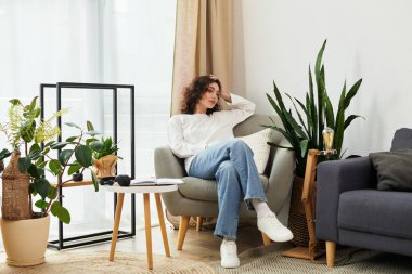 Kıvırcık kahverengi saçlı genç bir kadın çağdaş yaşam alanında biraz dinleniyor..