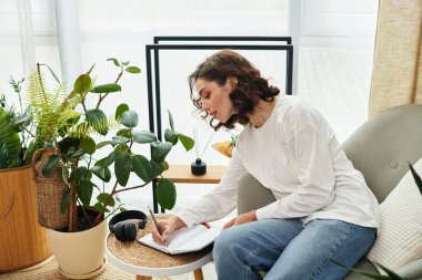 Kıvırcık saçlı kadın günlükleri şık, bitkilerle dolu dairesinde rahat bir koltukta..