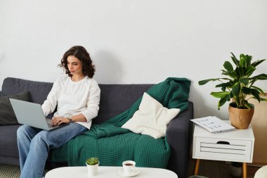 Kıvırcık saçlı genç bir kadın, konforlu evinde uzaktan kumandalı iş yapıyor..