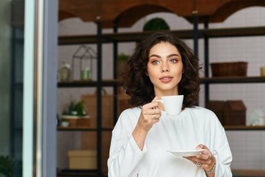 Kıvırcık saçlı genç bir kadın modern dairesinde dinleniyor ve çayını yudumluyor..