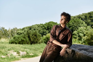 Kıvırcık saçlı genç adam bir parkta şık bir yaz elbisesinde rahatlıyor..