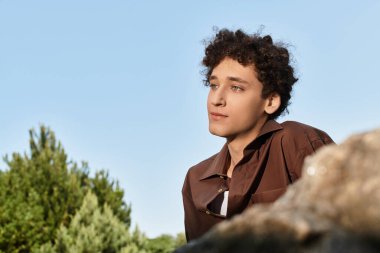 Kıvırcık saçlı genç bir adam, şık bir yaz kıyafeti içinde parkta rahatlar..