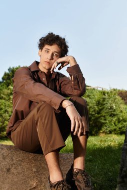 Kıvırcık saçlı genç adam, açık havada bir yaz gününün sıcağında ıslanırken taşın üzerinde rahatlar..