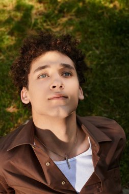 Kıvırcık saçlı genç bir adam enerjik bir parkta güneşli bir günün tadını çıkarıyor..