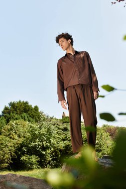 Moda kıyafetli kendine güvenen genç bir adam güneşin altındaki yemyeşil bir parkta dinleniyor..