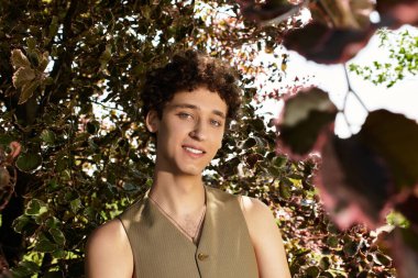 Parlak güneş ışığı kıvırcık saçlı genç bir adamın parlak bir parkta dinlendiğini vurguluyor..