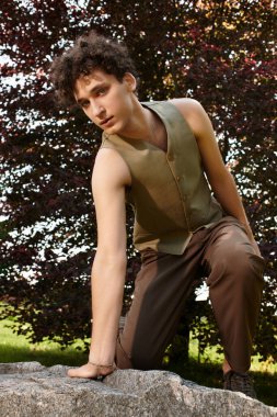 Kıvırcık saçlı genç bir adam, şık bir yaz elbisesi içinde yemyeşil bir parkı keşfediyor..