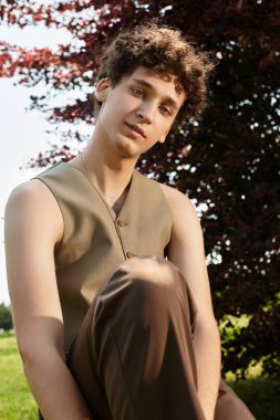 Kıvırcık saçlı genç bir adam yeşil bir parkta rahatlıyor, son moda bir yaz havası ve havası var..