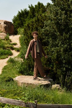 Kıvırcık saçlı, şık yaz kıyafetli bir adam parkın doğal yolunda yürüyor..