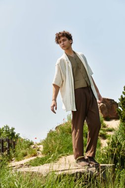 Yeşil bir parkta kendine güvenen genç bir adam moda kıyafetlerini sergiliyor..