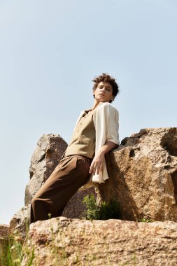 Kıvırcık saçlı genç bir adam güneşli bir parkta, şık bir yaz kıyafetiyle hava atıyor..