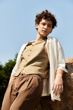 Kıvırcık saçlı genç adam güneşli bir parkta rahatlıyor, gösterişli yaz tarzı..