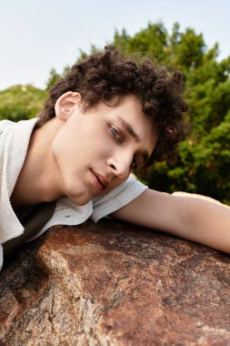 Kıvırcık saçlı genç bir adam yemyeşil bir parkta gevşeyip yazın sıcaklığını kucaklıyor..