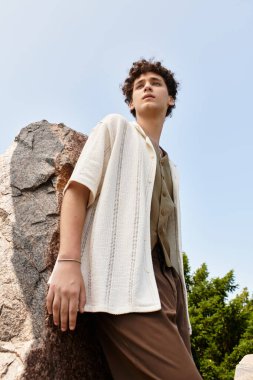 Kıvırcık saçlı genç adam dışarıda dinleniyor, etrafında sıcak güneş ışığını ve doğayı kucaklıyor..