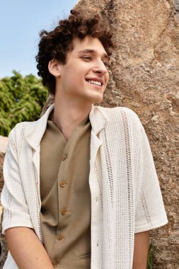 Kıvırcık saçlı genç adam canlı yeşil bir parkta güneşli bir günün tadını çıkarıyor. Doğanın güzelliğini kucaklıyor..