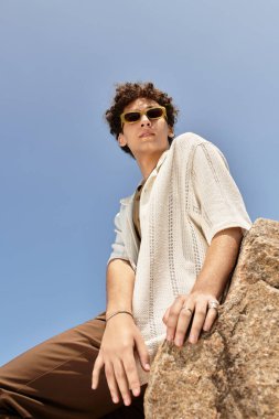 Kıvırcık saçlı genç bir adam yeşil bir parkta güneşli bir günde moda anlayışını sergiliyor..