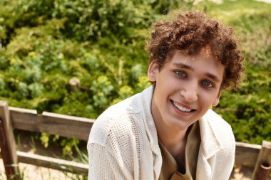 Kıvırcık saçlı genç adam, lüks bir parkta rahat rahat güneşleniyor..