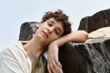 Kıvırcık saçlı genç adam dışarıda, parkta güneşlenirken şık yaz kıyafetlerini sergiliyor..