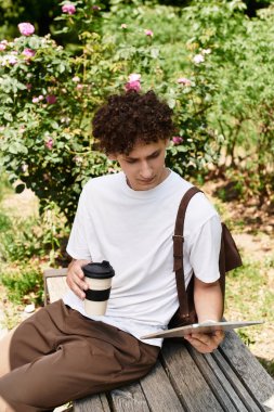 Genç bir adam yemyeşil bir parktaki bankta rahatlar, kahvesini yudumlar ve kitap okur..