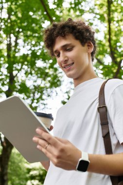 Genç bir adam yazları yemyeşil bir ortamda kahvesini yudumlarken tabletine bağlanır..