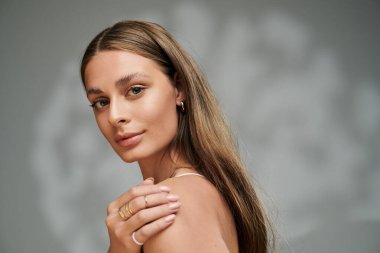 Işıl ışıl bir sıcaklık ve güven saçan genç bir kadın, yazın gri bir zemine hafifçe poz veriyor..