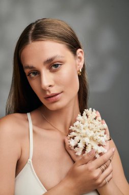 Bronz tenli ve doğal makyajlı genç bir kadın yaz stüdyosunda mercanlarla poz veriyor..