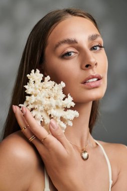 Bronz tenli ve doğal makyajlı genç bir kadın stüdyoda mercanlarla zarifçe poz veriyor..