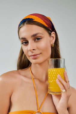 Bronz tenli ve başörtülü genç bir kadın ferahlatıcı bir içecekle rahatça poz veriyor..