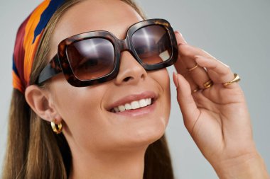 Parlak stüdyo, güneş gözlüğünü ayarlarken bronz tenli gülümseyen genç bir kadını yakalıyor..