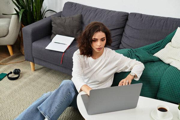 Молодая женщина с вьющимися волосами фокусируется на своем ноутбуке, работая из своего комфортного дома.