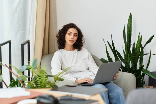 Красивая женщина с кудрявыми волосами сосредоточена на своем ноутбуке, работая из дома.