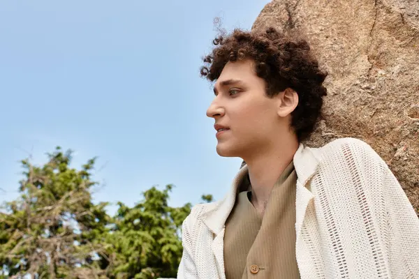 Kıvırcık saçlı genç bir adam yeşilliğin ortasında gevşiyor ve yaz modasının neşesini kucaklıyor..